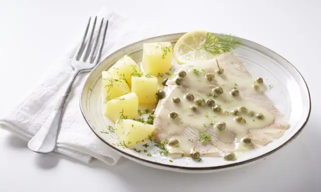 Une aile de raie nappée d'une sauce crémeuse aux câpres, accompagnée de pommes de terre et d'une tranche de citron.