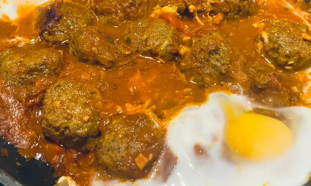 Un plat de tajine kefta oeuf mijote dans une sauce tomate épicée, avec des œufs pochés.