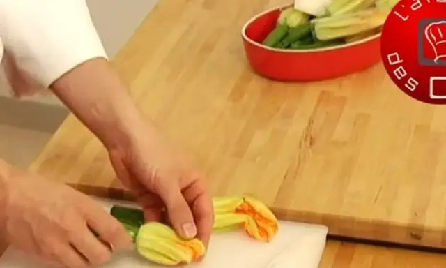 Préparation d'une fleur de courgette recette. Des mains préparent des fleurs de courgette sur une planche à découper.
