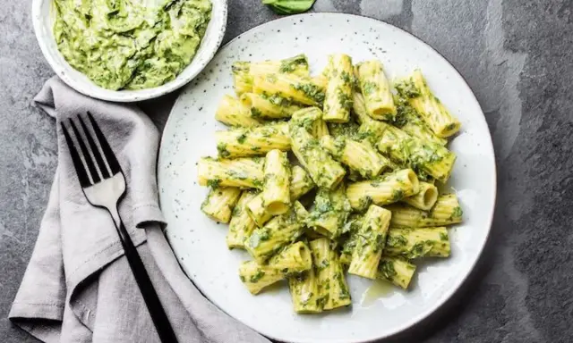 Assiette de pâtes rigatoni généreusement enrobées de pesto vert vif, avec un bol de sauce à côté. Un délice de pâtes au pesto !
