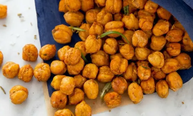 Un tas de pois chiches grillés dorés, certains tombant d'un sac bleu, avec des brins de romarin.