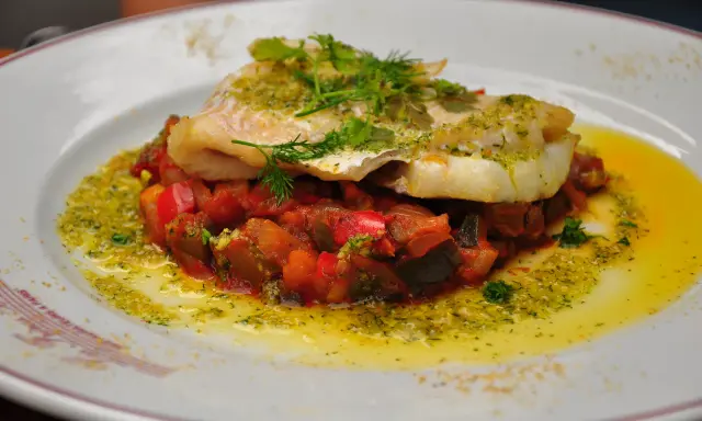 Délicieux dos de cabillaud à la poêle, servi sur un lit de légumes méditerranéens et arrosé d'une sauce verte.