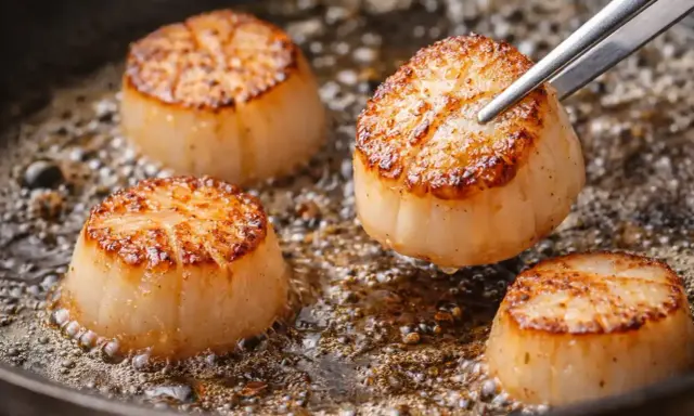 Quatre belles coquilles Saint-Jacques poêlées dans une poêle, dorées et juteuses, prêtes à être dégustées.