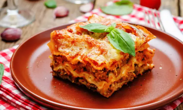 Une part généreuse de lasagne végétarienne, dorée au four, garnie de basilic frais, sur une assiette en terre cuite.