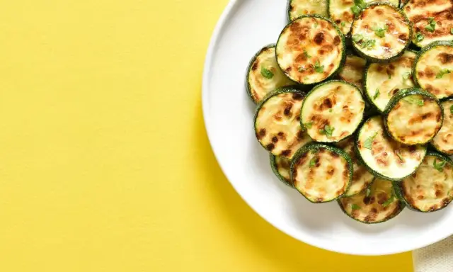 Courgettes rondes grillées à l'air fryer, parsemées d'herbes fraîches, sur une assiette blanche, sur fond jaune vif.