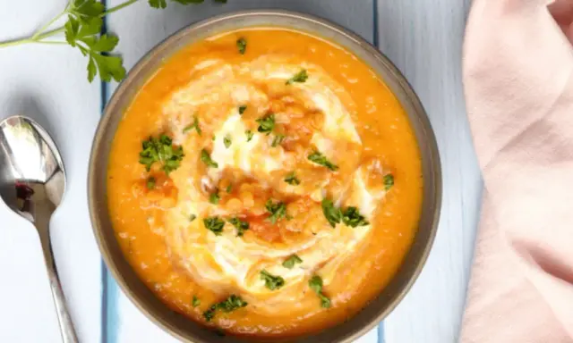 Un bol de soupe crémeuse aux lentilles corail, garni de crème et de persil frais, prêt à être dégusté avec une cuillère.