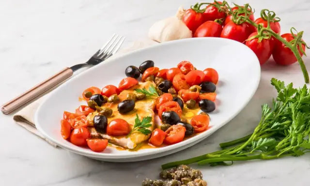 Filet de merlan servi avec tomates cerises, olives noires et câpres. Une assiette colorée et savoureuse.