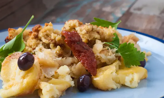 Morue à bras, un plat réconfortant avec des flocons de poisson, des olives noires, des tomates séchées et une touche de persil frais.
