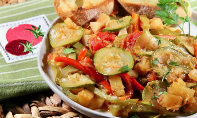 Un plat de légumes mijotés, rappelant un pisto manchego, avec des courgettes, poivrons et tomates, servi avec des toasts grillés.