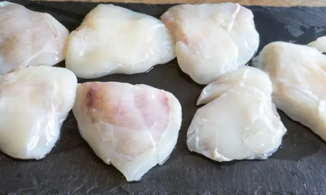 Plusieurs morceaux de lotte crue, prêts pour une cuisson au four, sont disposés sur une planche d'ardoise.