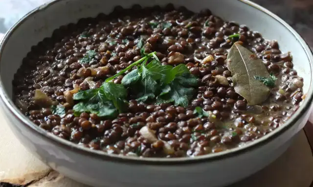 Un plat de cuisson lentilles vertes, garni de persil frais et d'une feuille de laurier. Un délice simple et réconfortant.