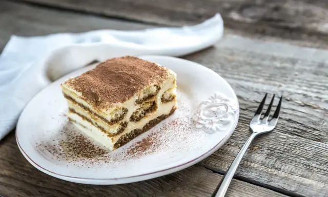 Une part de tiramisu maison, saupoudrée de cacao, sur une assiette blanche, prête à être dégustée. La conservation de ce délice est essentielle pour en savourer chaque bouchée.