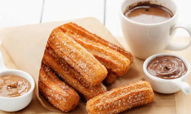 Churros dorés et croustillants, saupoudrés de sucre, prêts à être trempés dans le chocolat. Une recette gourmande pour un goûter parfait.
