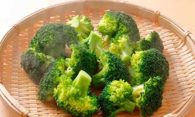 Brocolis coupés en bouquets dans un panier en osier, prêts pour la cuisson. La vapeur s'échappe, signe d'une cuisson à la vapeur parfaite.