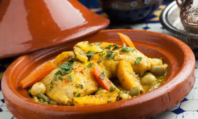 Un plat de tajine recette traditionnelle, avec du poulet, des carottes, des olives et des abricots, garni de persil frais.