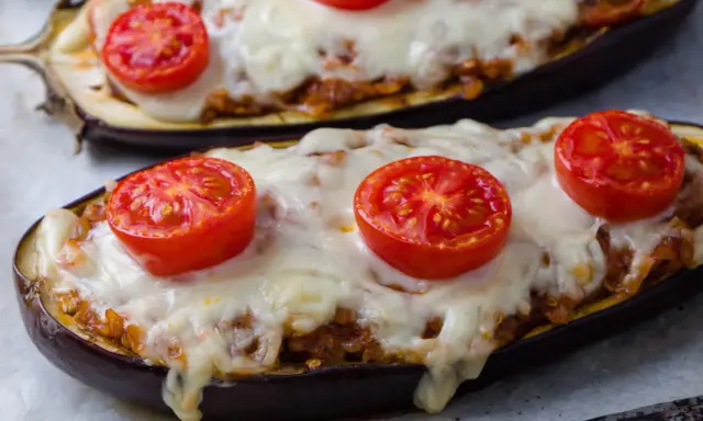 Deux aubergines farcies, garnies de tomates et de fromage fondu, prêtes à être dégustées.