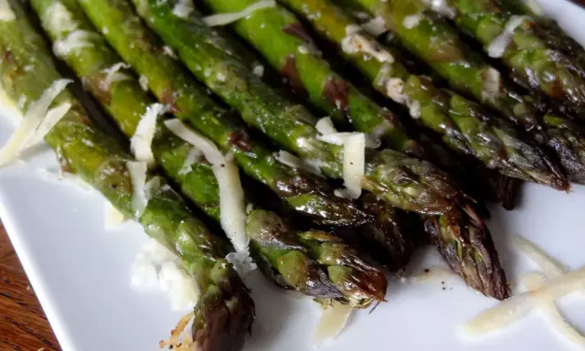 Un plat d'asperges au four, tendres et légèrement grillées, parsemées de copeaux de parmesan. Un délice simple et savoureux.