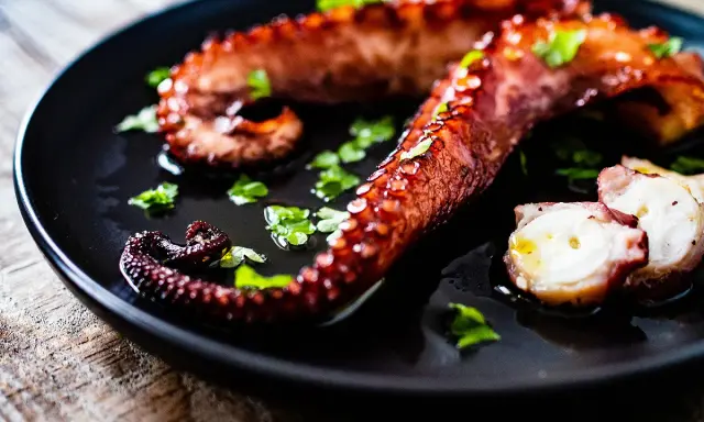 Tentacules de poulpe grillés, parsemés de persil frais, prêts à être dégustés. Une recette poulpe simple et savoureuse.