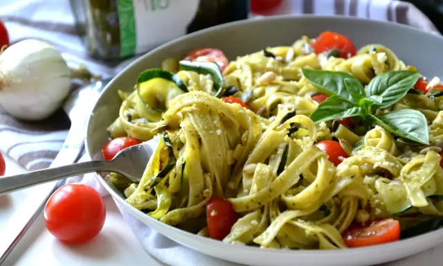 Un plat de tagliatelles de courgettes, tomates cerises et pesto, garni de basilic frais et de pignons de pin.