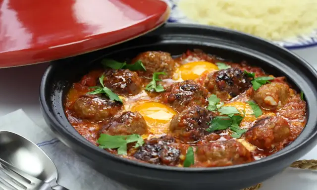 Un savoureux tajine kefta avec des boulettes de viande et des œufs pochés dans une sauce tomate épicée, garni de persil frais.