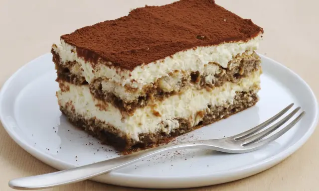 Une part de tiramisu sans oeuf, légère et aérienne, saupoudrée de cacao, sur une assiette blanche avec une fourchette.