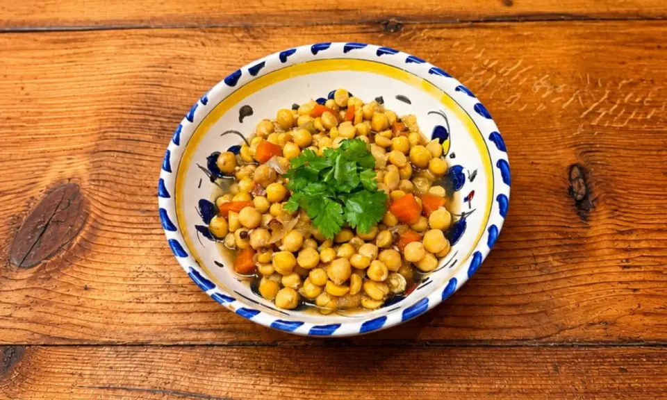 Un plat de pois chiches cuisinés avec des carottes et des oignons, garni de coriandre fraîche. La cuisson pois chiche est réussie, le plat est appétissant.