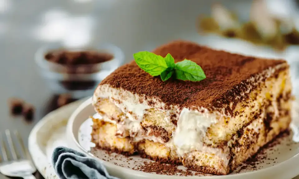 Un délicieux tiramisu anniversaire, saupoudré de cacao et garni d'une feuille de menthe fraîche, prêt à être dégusté.