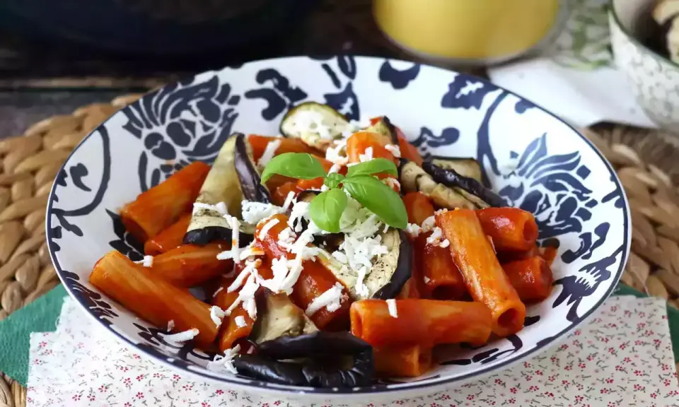 Pâtes rigatoni généreusement garnies de sauce tomate, d'aubergines grillées et de fromage râpé, le tout surmonté d'une feuille de basilic frais. Un plat de pâtes aubergines appétissant.