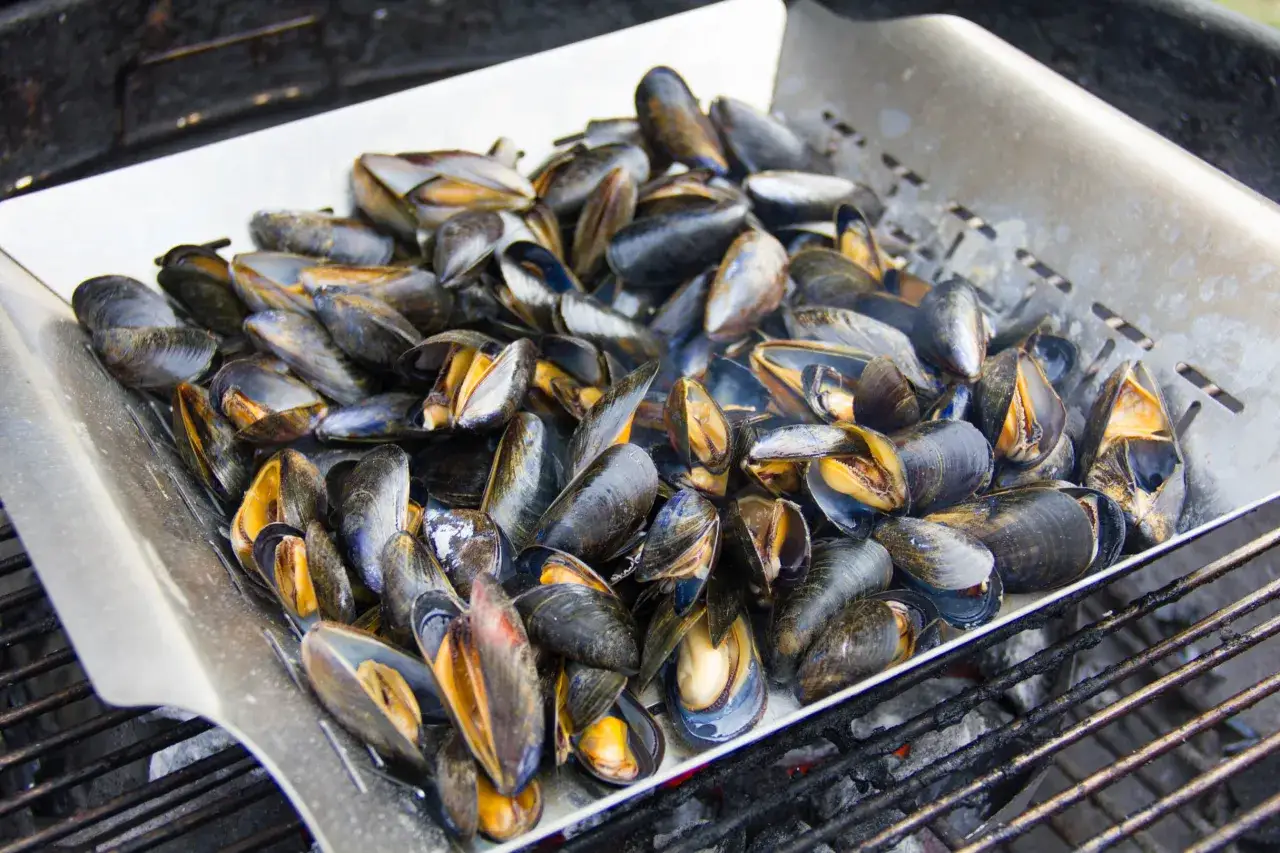 Un plateau rempli de moules au barbecue, pr&ecirc;tes &agrave; &ecirc;tre d&eacute;gust&eacute;es. Les coquilles sombres contrastent avec la chair orang&eacute;e.
