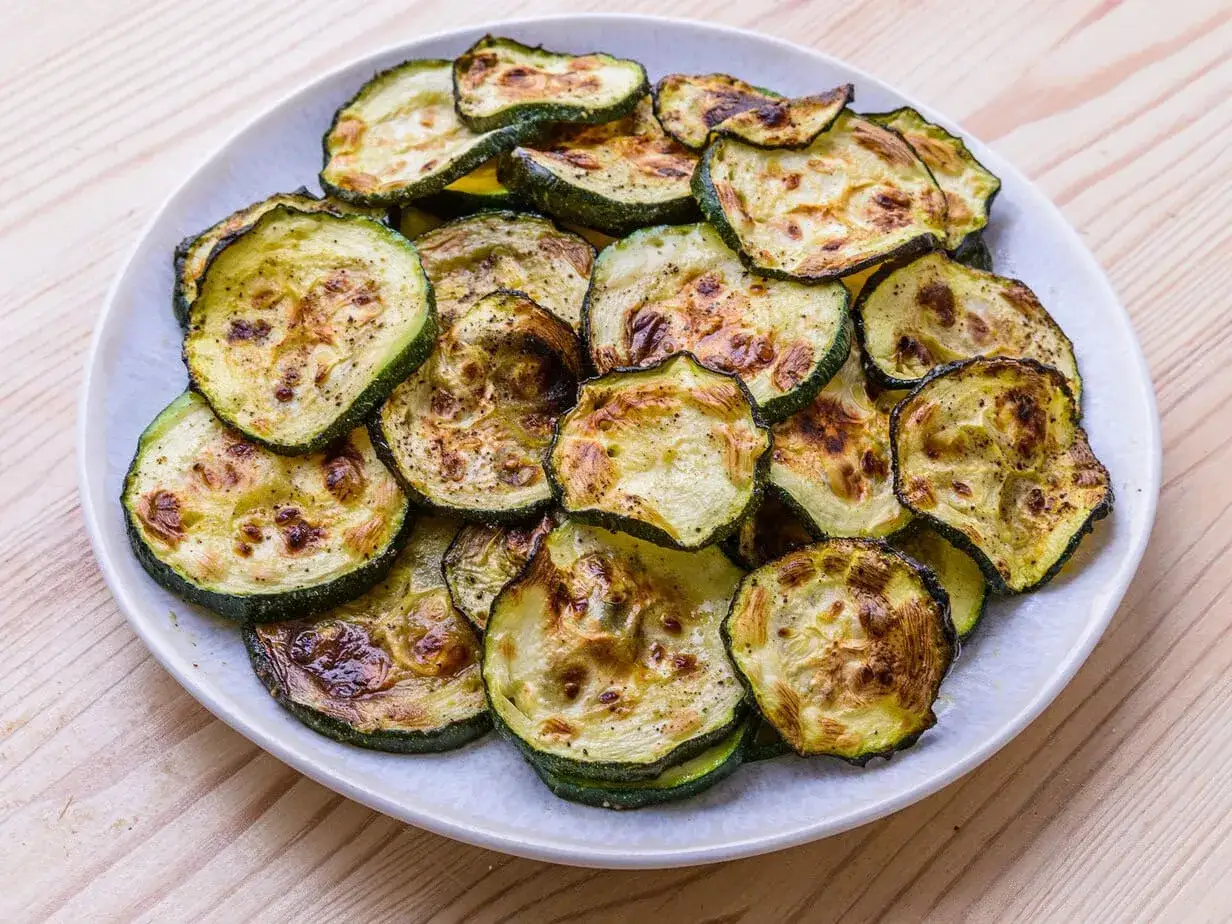 Tranches de courgette grill&eacute;es &agrave; l'air fryer, l&eacute;g&egrave;rement dor&eacute;es et assaisonn&eacute;es, pr&eacute;sent&eacute;es sur une assiette blanche.