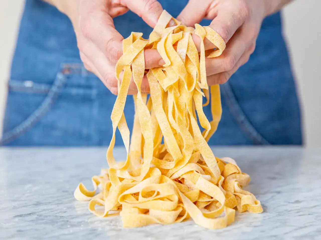Des mains tiennent des pâtes fraîches, prêtes à être cuisinées. Un aperçu de comment faire des pâtes maison.