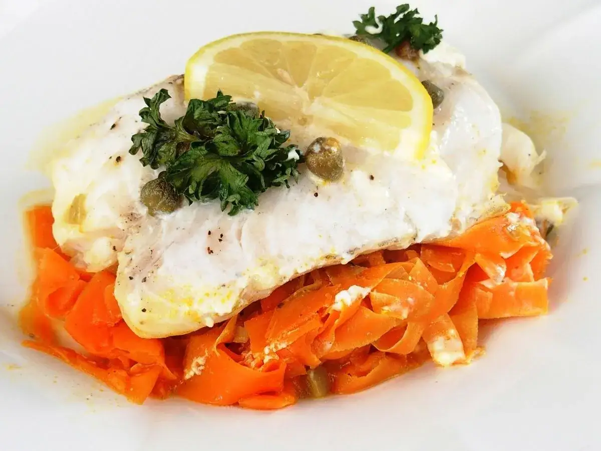 D&eacute;licieux cabillaud en papillote, servi sur des carottes r&acirc;p&eacute;es, garni de persil, c&acirc;pres et d'une tranche de citron.