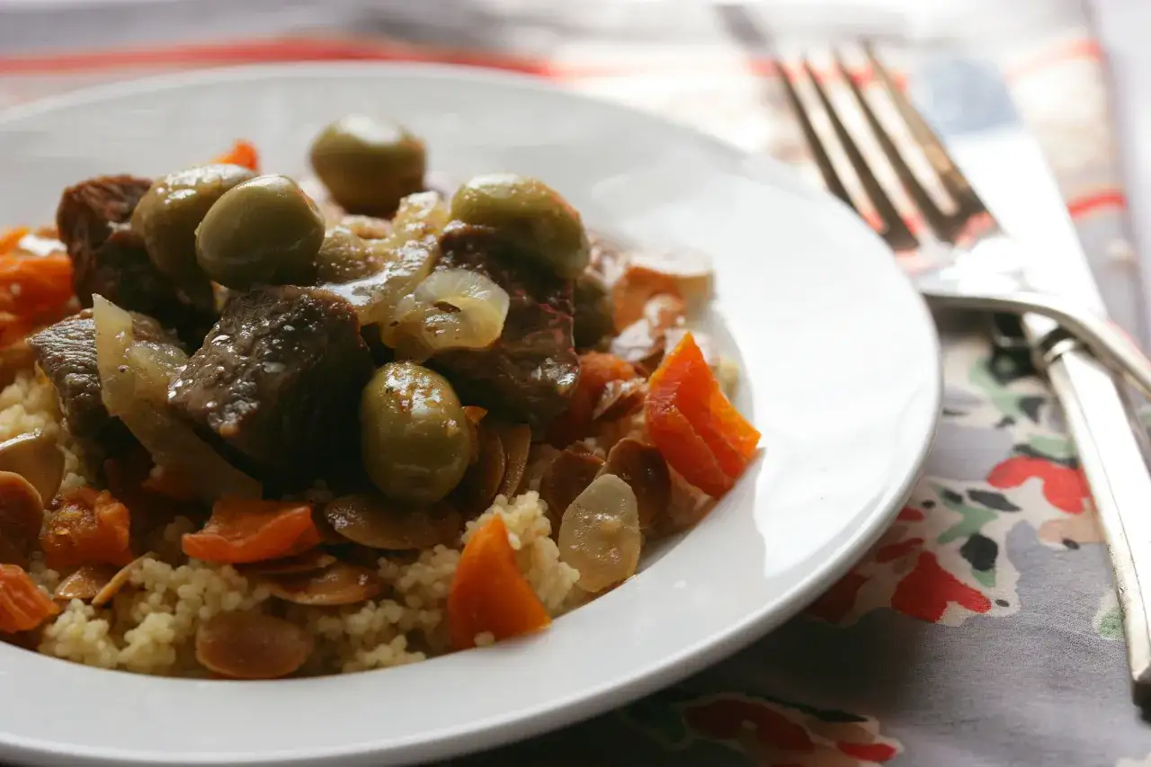 Un plat de tajine agneau savoureux avec des olives, des abricots secs et des amandes effil&eacute;es sur un lit de couscous.