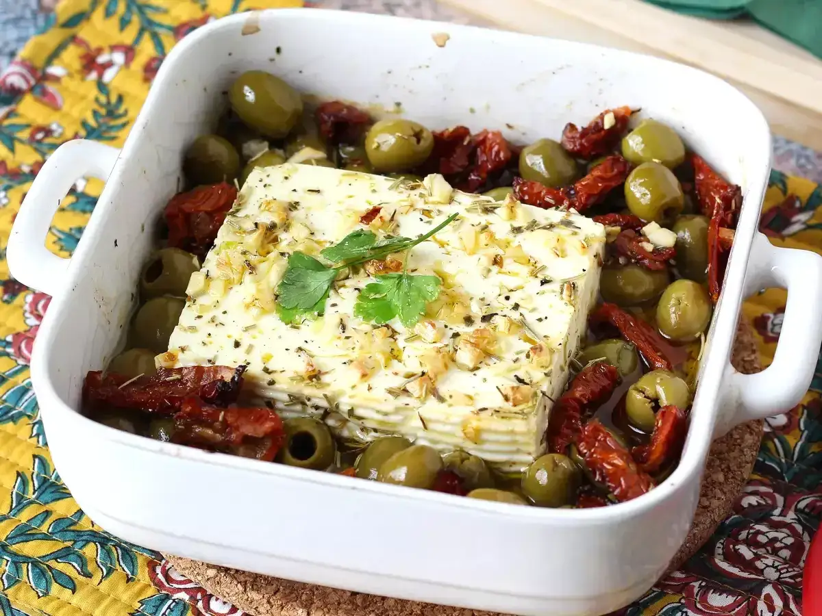 Un bloc de feta cuit au four, entour&eacute; d'olives vertes et de tomates s&eacute;ch&eacute;es. Une recette simple et savoureuse avec feta.