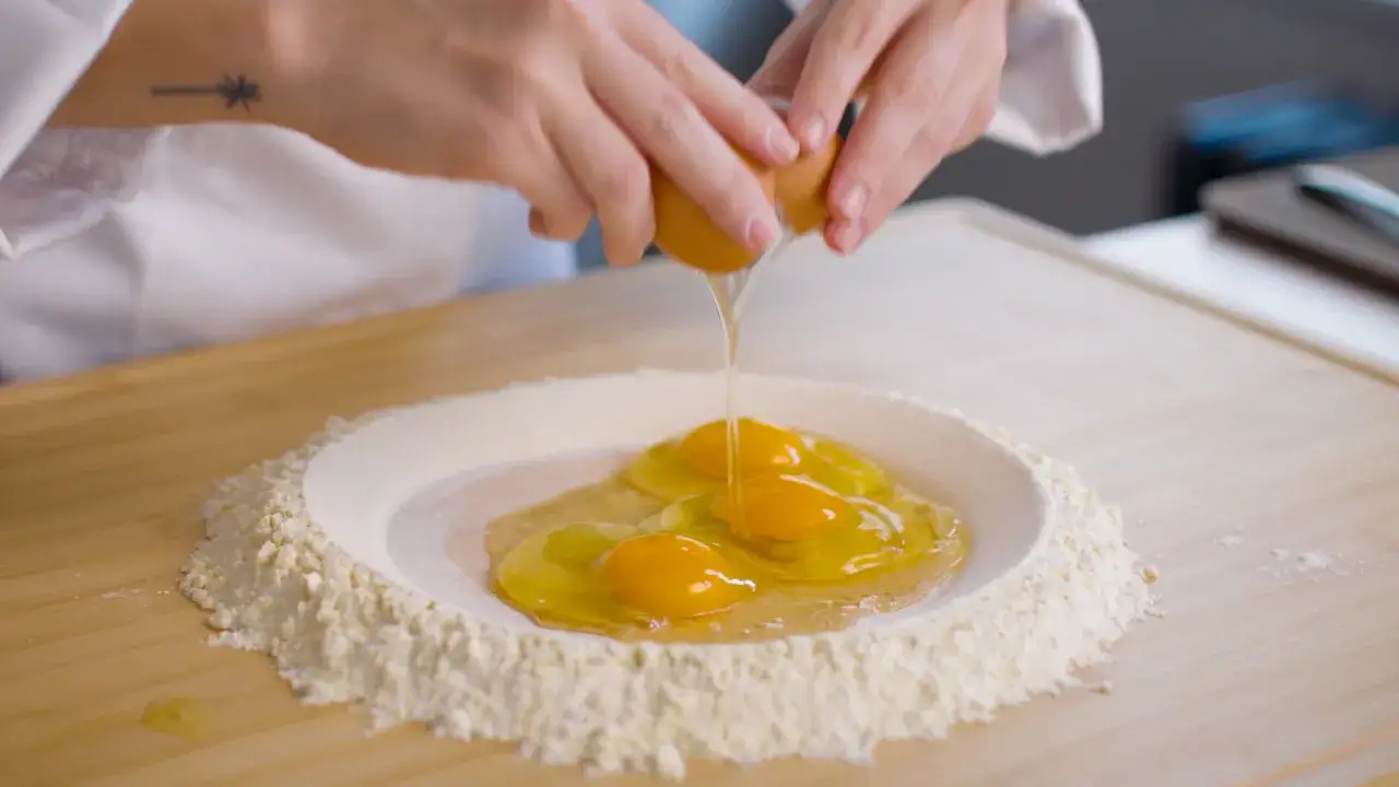 Des &oelig;ufs tombent dans un puits de farine pour p&acirc;tes italiennes, pr&ecirc;ts &agrave; &ecirc;tre m&eacute;lang&eacute;s pour une p&acirc;te maison.