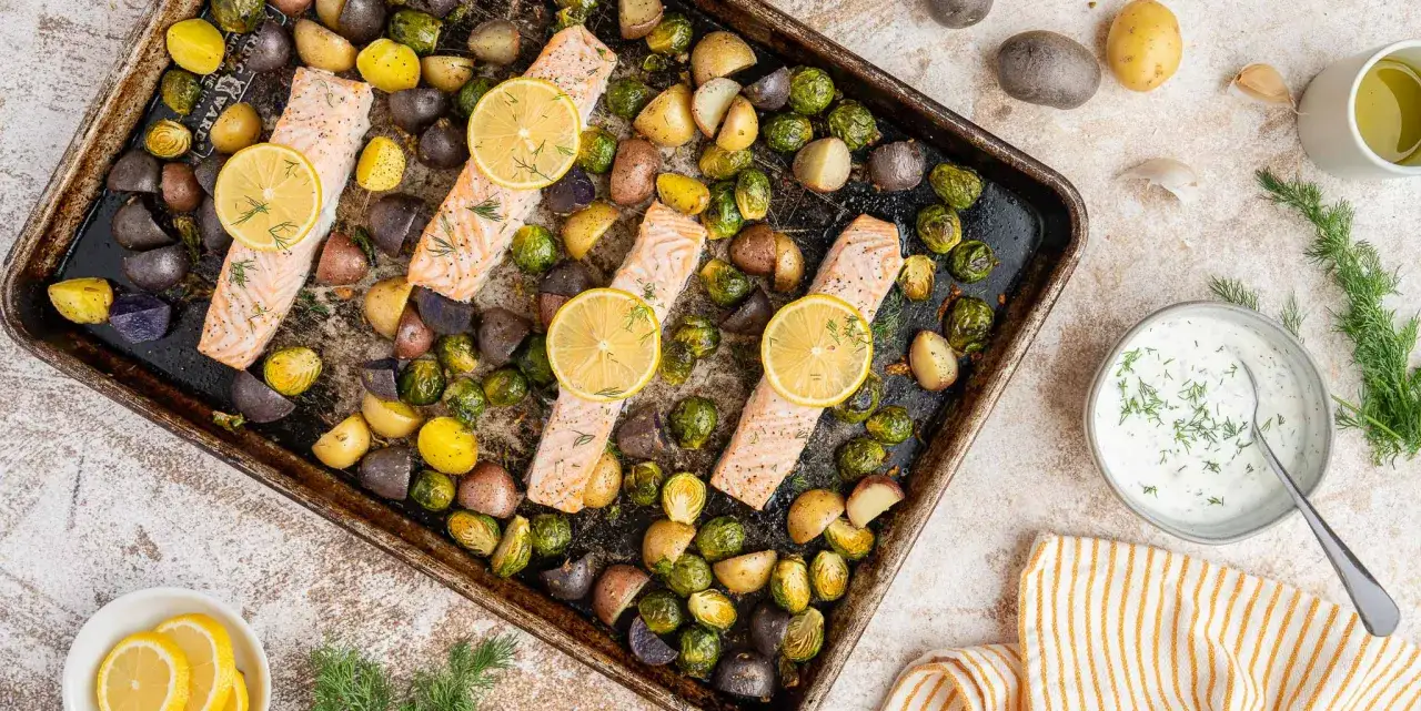 Quatre filets de saumon au four, garnis de rondelles de citron et d'aneth, accompagn&eacute;s de pommes de terre r&ocirc;ties et de choux de Bruxelles sur une plaque.