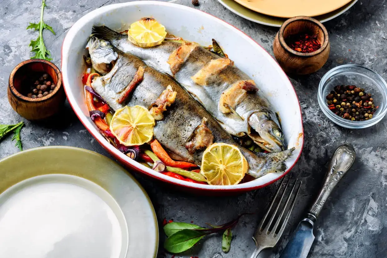 Deux truites enti&egrave;res r&ocirc;ties avec des citrons et des l&eacute;gumes, pr&ecirc;tes pour une d&eacute;licieuse recette truite.