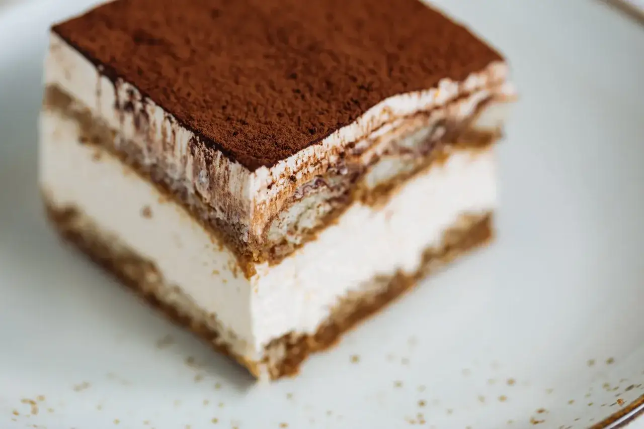 Une part de tiramisu sans oeuf, l&eacute;g&egrave;re et a&eacute;rienne, saupoudr&eacute;e de cacao, sur une assiette blanche.
