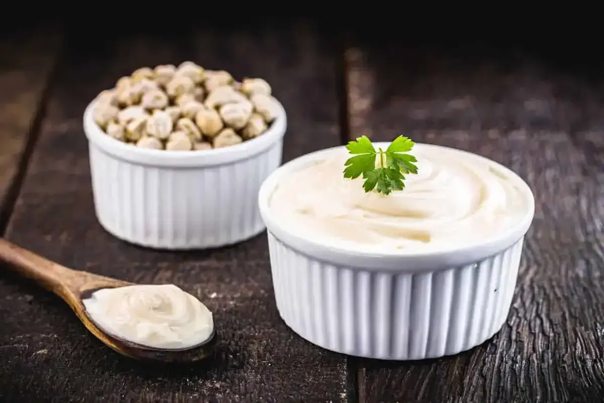 Cr&egrave;me onctueuse dans un ramequin, garnie de persil. &Agrave; c&ocirc;t&eacute;, des pois chiches secs et une cuill&egrave;re de cette pr&eacute;paration cr&eacute;meuse, peut-&ecirc;tre faite avec de l'eau de pois chiche.