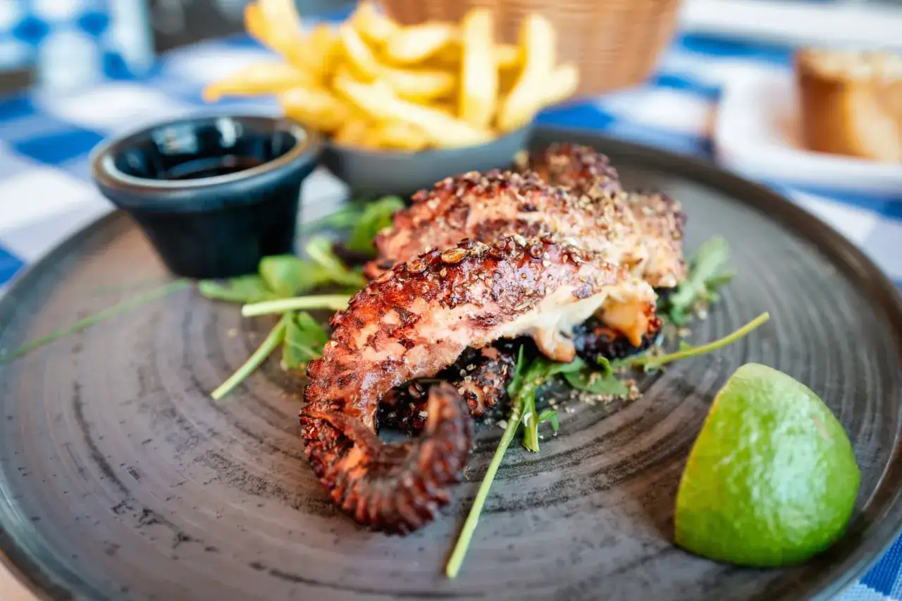 D&eacute;licieux poulpe au barbecue, servi avec des frites croustillantes, une sauce et un quartier de citron vert. Un vrai r&eacute;gal !