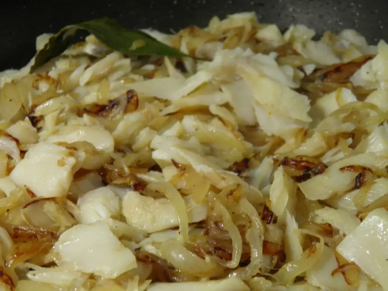 Morue &agrave; bras, un plat r&eacute;confortant de poisson effiloch&eacute; et d'oignons caram&eacute;lis&eacute;s, avec une feuille de laurier.
