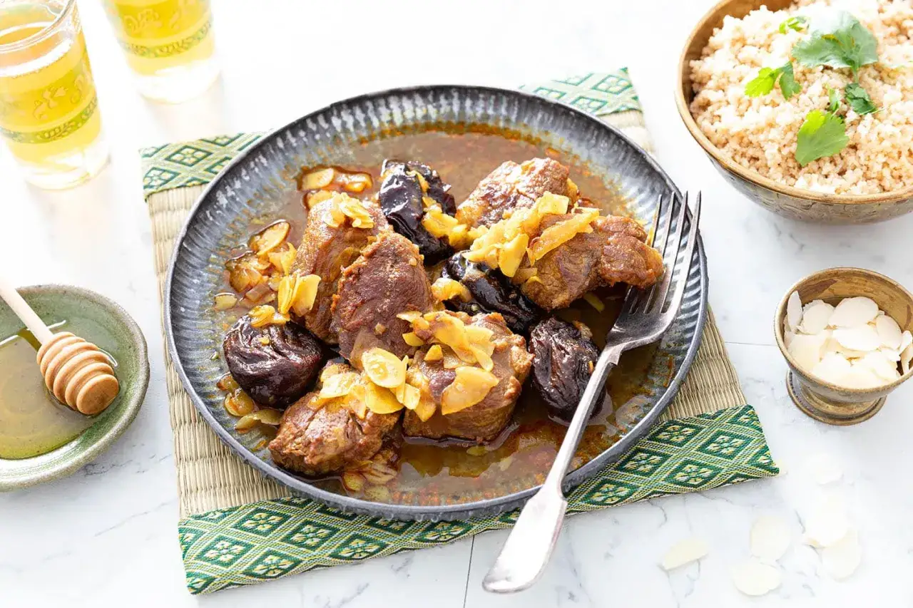 Un plat savoureux de tajine aux pruneaux, garni d'amandes effil&eacute;es, servi avec du couscous et du miel.