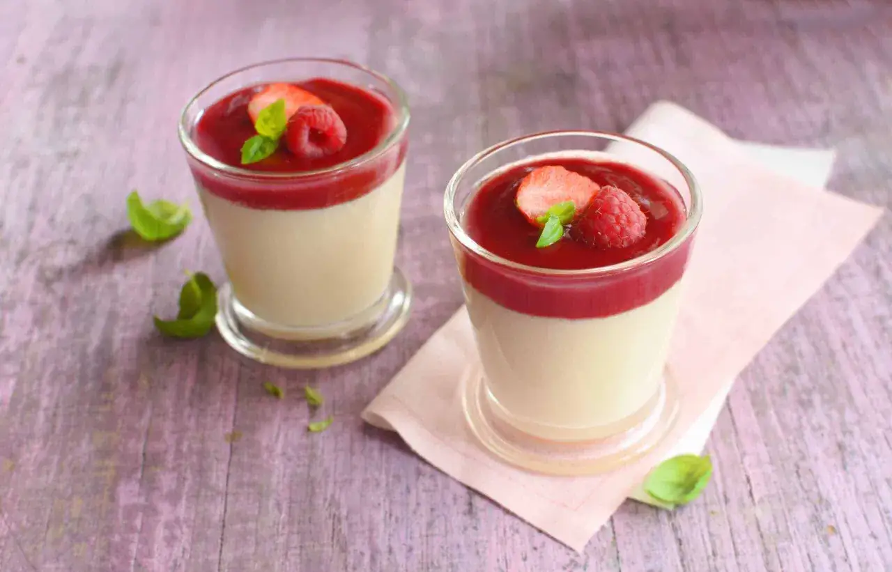 Deux panna cotta au lait sans crème, garnies de fruits rouges et de menthe, sur une table en bois.