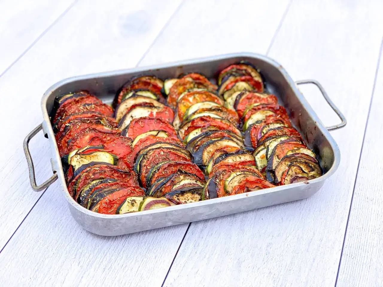 Un plat de tian de l&eacute;gumes, avec des rondelles de tomates, courgettes et aubergines dispos&eacute;es joliment dans un plat allant au four.