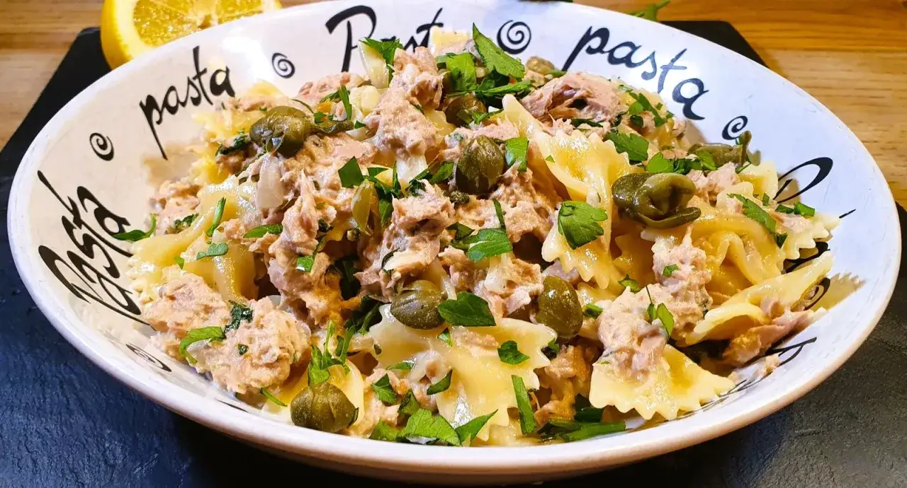 Un plat de p&acirc;tes au thon, garni de c&acirc;pres et de persil frais, servi dans un bol d&eacute;cor&eacute; du mot 