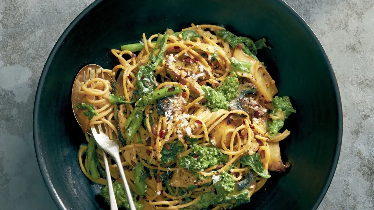 Un plat de p&acirc;tes carbonara vege, garni de brocolis, champignons et flocons de piment rouge, servi dans un bol noir avec une fourchette.