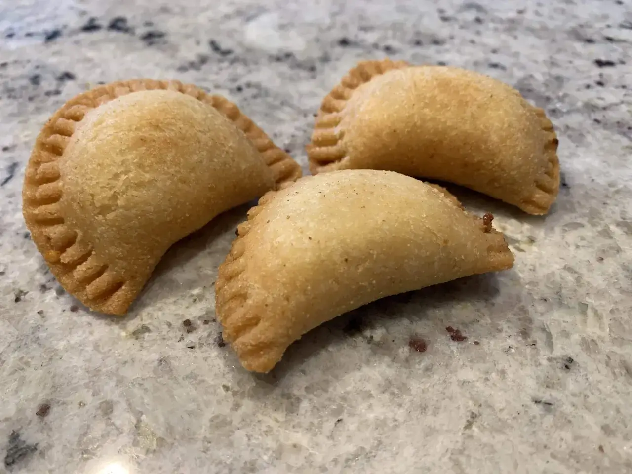 Trois samboussek fromage dorés, prêts à être dégustés, sur un plan de travail marbré.