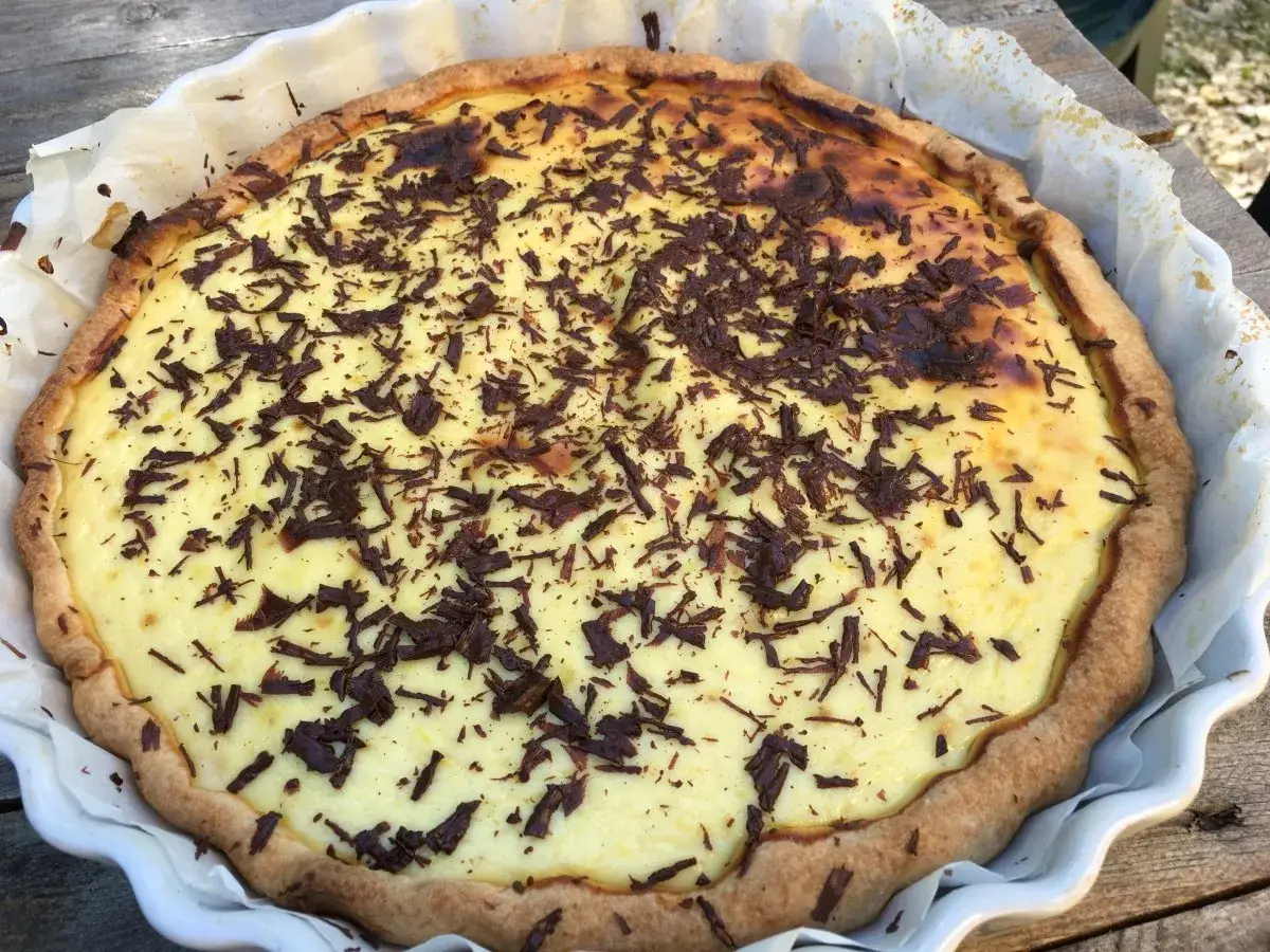 G&acirc;teau &agrave; la ricotta sicilien, garni de copeaux de chocolat noir, dans un plat blanc sur une table en bois.