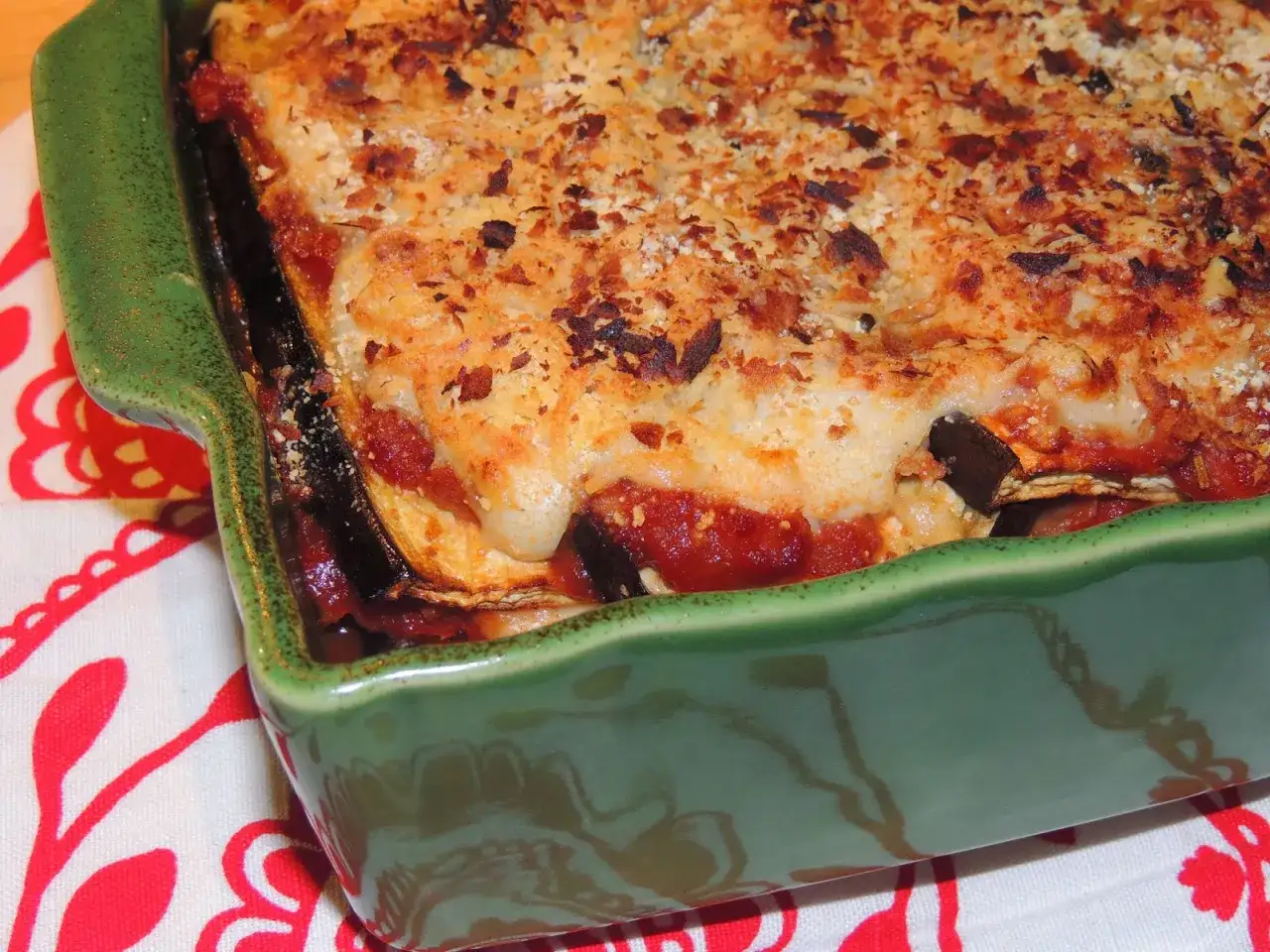 Un plat de moussaka v&eacute;g&eacute;tarienne gratin&eacute;e, avec des couches d'aubergines, de sauce tomate et de b&eacute;chamel, dans un plat vert.