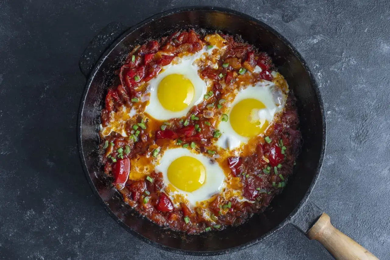 Po&ecirc;le de chakchouka maison, avec &oelig;ufs poch&eacute;s dans une sauce tomate et poivrons, garnie de ciboule. Une recette savoureuse.